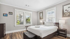Un dormitorio con una cama grande, dos mesitas de noche, un banco y un aparador.