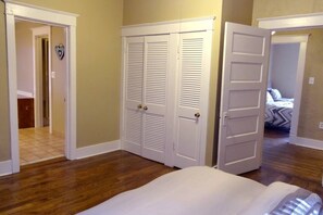 A bedroom with a wooden floor, a bed with white bedding, and a white closet with two doors.