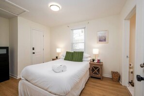 Une chambre d’hôtel avec un lit, deux tables de chevet, une fenêtre, une porte et un tableau accroché au mur.