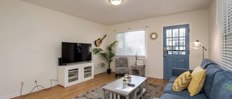 Una sala de estar con televisor, una mesa de centro, un sofá, un tapete estampado y una puerta con ventanal.