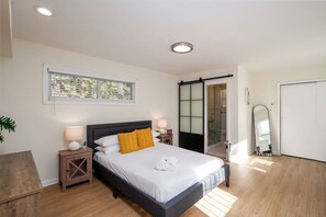 Une chambre moderne comprenant un lit, des tables de chevet, une fenêtre et une porte coulissante donnant sur une salle de bain.