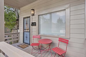 A covered porch with a red metal table and chairs, a door with a mailbox, and a window with blinds.