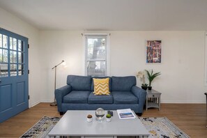 Un salon avec un canapé bleu, une table basse blanche, un lampadaire et un tableau accroché au mur.