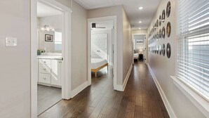 Un pasillo con suelo de madera, paredes blancas y una escalera que lleva a un dormitorio.