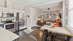 A modern kitchen with stainless steel appliances, a dining area with a marble table, and a living space with a sofa and coffee table.
