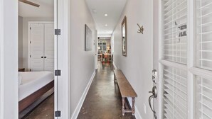 A narrow hallway with a wooden bench, white doors, and a dining area in the distance.