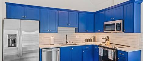 Una cucina con pensili azzurri, elettrodomestici in acciaio inox e un tavolo da pranzo in legno.