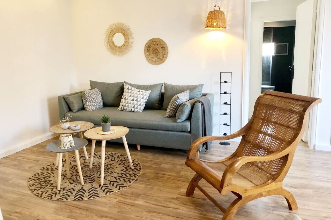 A living room with a grey sofa, two side tables, a wicker chair, and decorative wall art.
