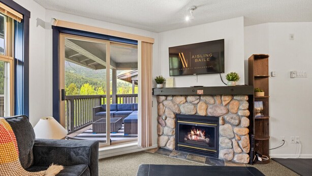 A living room with a stone fireplace, a television mounted above it, and a sliding glass door leading to an outdoor seating area.