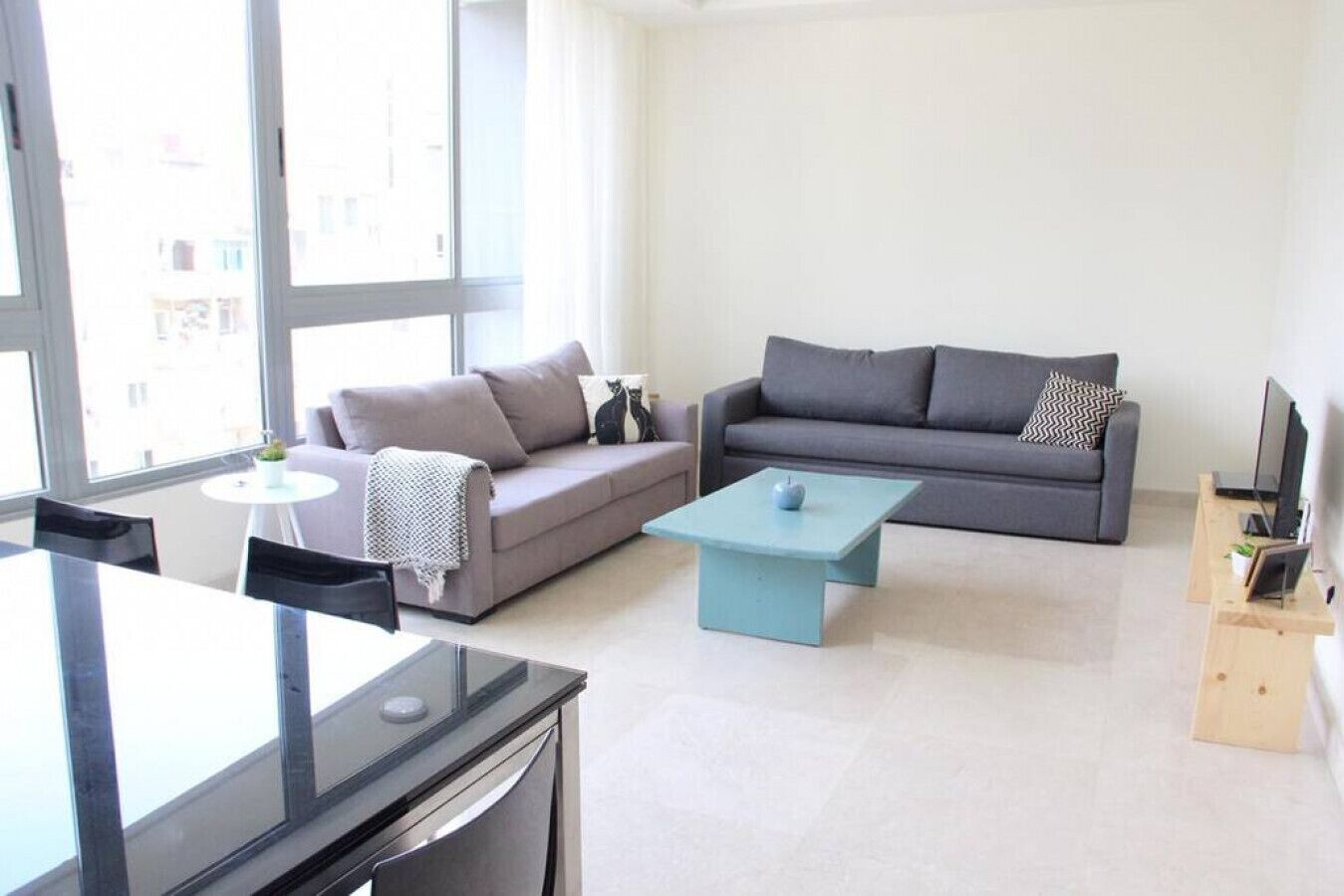 A modern living room with a grey sofa, a blue coffee table, and a dining area with a glass table and chairs.