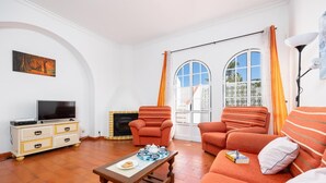 Ein Wohnzimmer mit Fernseher, Kamin, orange gestreiften Sofas und einem Tisch mit Teekanne.