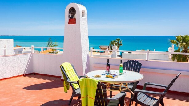 Eine Terrasse mit Tisch und Stühlen, eine weiße Säule und Blick auf das Meer.