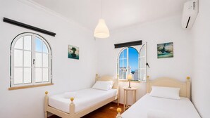 Ein Zimmer mit zwei Betten, einem Fenster, einer Lampe und einem Gemälde.