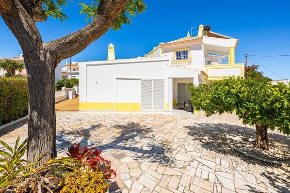 Une maison à deux étages, avec une façade blanche et des bordures jaunes, un garage et une allée pavée.