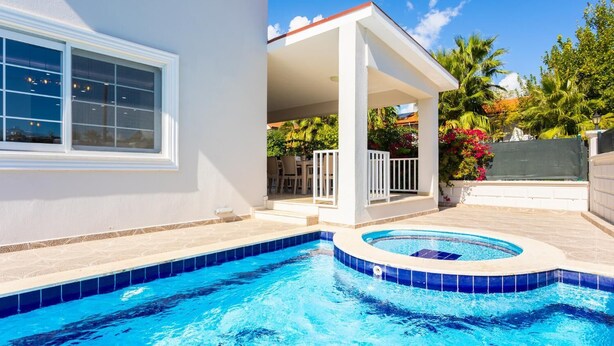 A swimming pool with a tiled edge, a covered patio area, and a view of a cityscape at dusk. - Villa Capital - Five Bedroom Villa, Sleeps 10 (Dalyan)