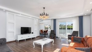 A modern living room with a television, white console, and a dining area with chairs and a table. - Villa Capital - Five Bedroom Villa, Sleeps 10 (Dalyan)