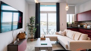 Een moderne woonkamer met een bank, salontafel en een aan de muur bevestigde televisie. Er staat een plant en er is een raam met gordijnen.