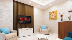 A modern living room with a Netflix TV, a clock, and a wooden panel wall. - Stunning 4BR Villa w/ Heated Jacuzzi in St. Paul's (San Pawl il-Bahar)