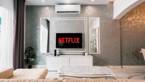 A modern living room with a large flat-screen TV displaying "NETFLIX" on the screen, a white entertainment unit, a potted plant, and a beige sofa. - Stunning 4BR Villa w/ Heated Jacuzzi in St. Paul's (San Pawl il-Bahar)