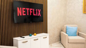 A room with a television displaying "NETFLIX" in red letters, a white cabinet with drawers, and a beige armchair with a blue pillow. - Stunning 4BR Villa w/ Heated Jacuzzi in St. Paul's (San Pawl il-Bahar)