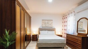 A bedroom with a large bed, wooden wardrobe, and a map on the wall. - A pretty holiday home in Malta’s fishing village (Marsaxlokk)