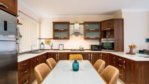 A modern kitchen with wooden cabinets, a stainless steel refrigerator, a microwave, and a gas stove. - A pretty holiday home in Malta’s fishing village (Marsaxlokk)