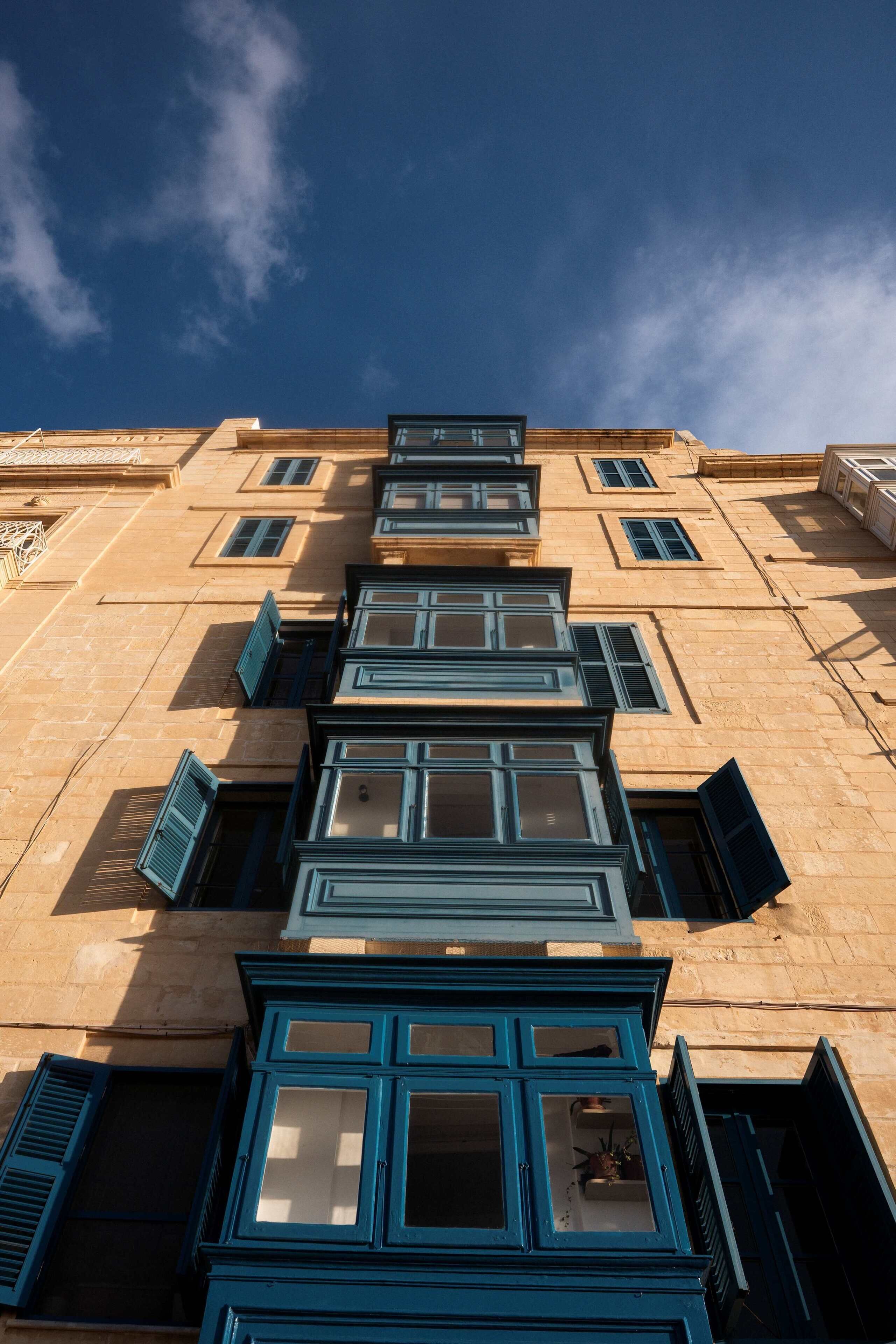 Un edificio de varios pisos con una serie de ventanas y contraventanas, algunas de las cuales están abiertas.