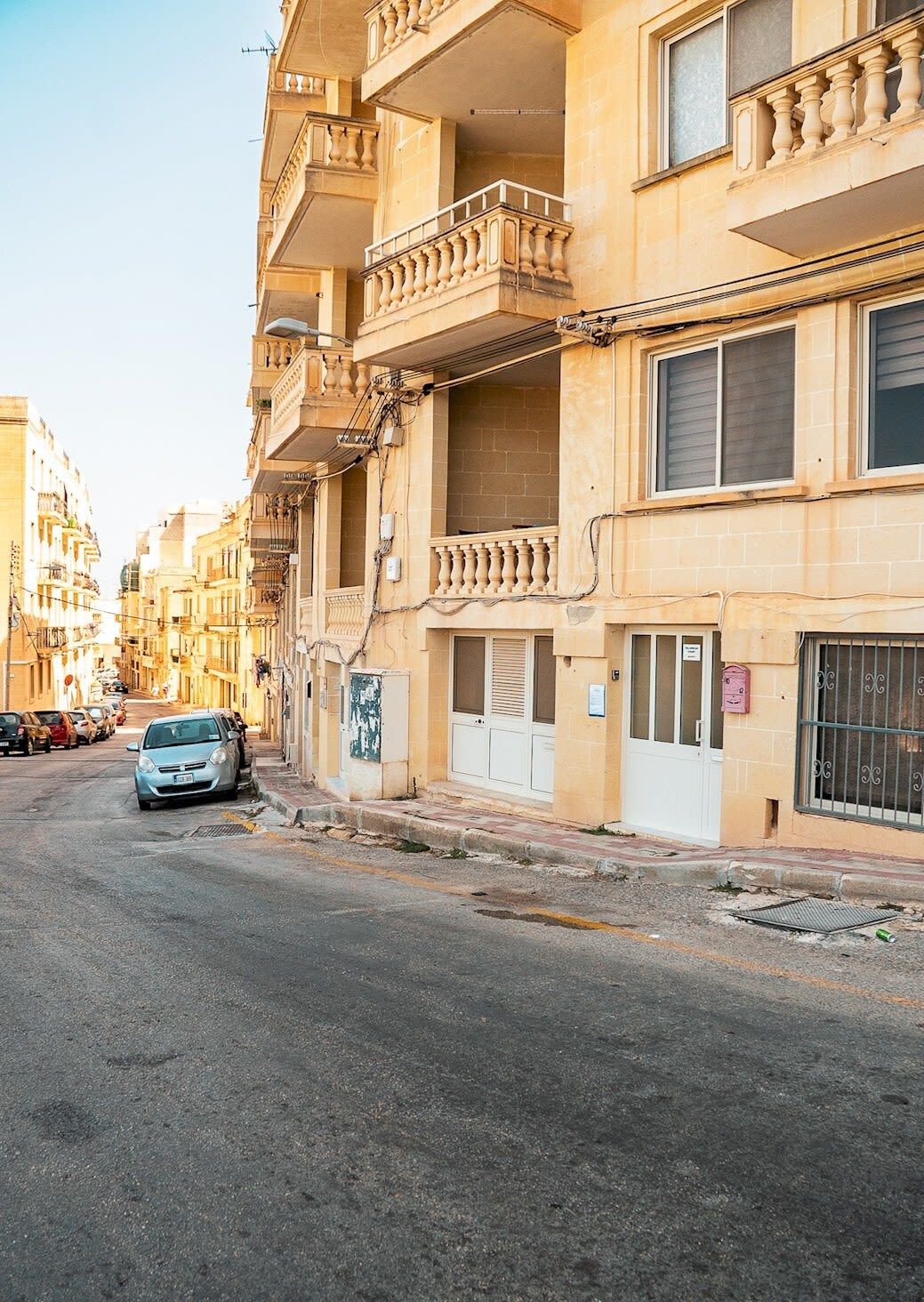 A multi-story building with balconies, a parked car, and a narrow street.