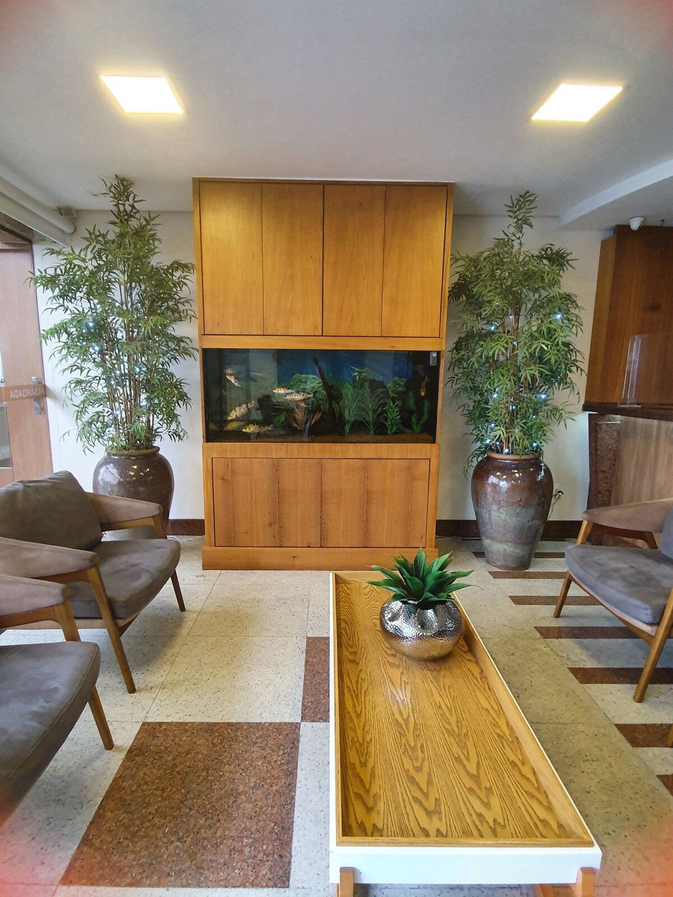 A modern living room with a wooden cabinet, two potted plants, a fish tank, and a wooden coffee table.