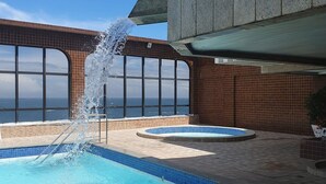 Une piscine agrémentée d’un élément décoratif aquatique, une vue sur l’océan et un bâtiment doté de grandes fenêtres.