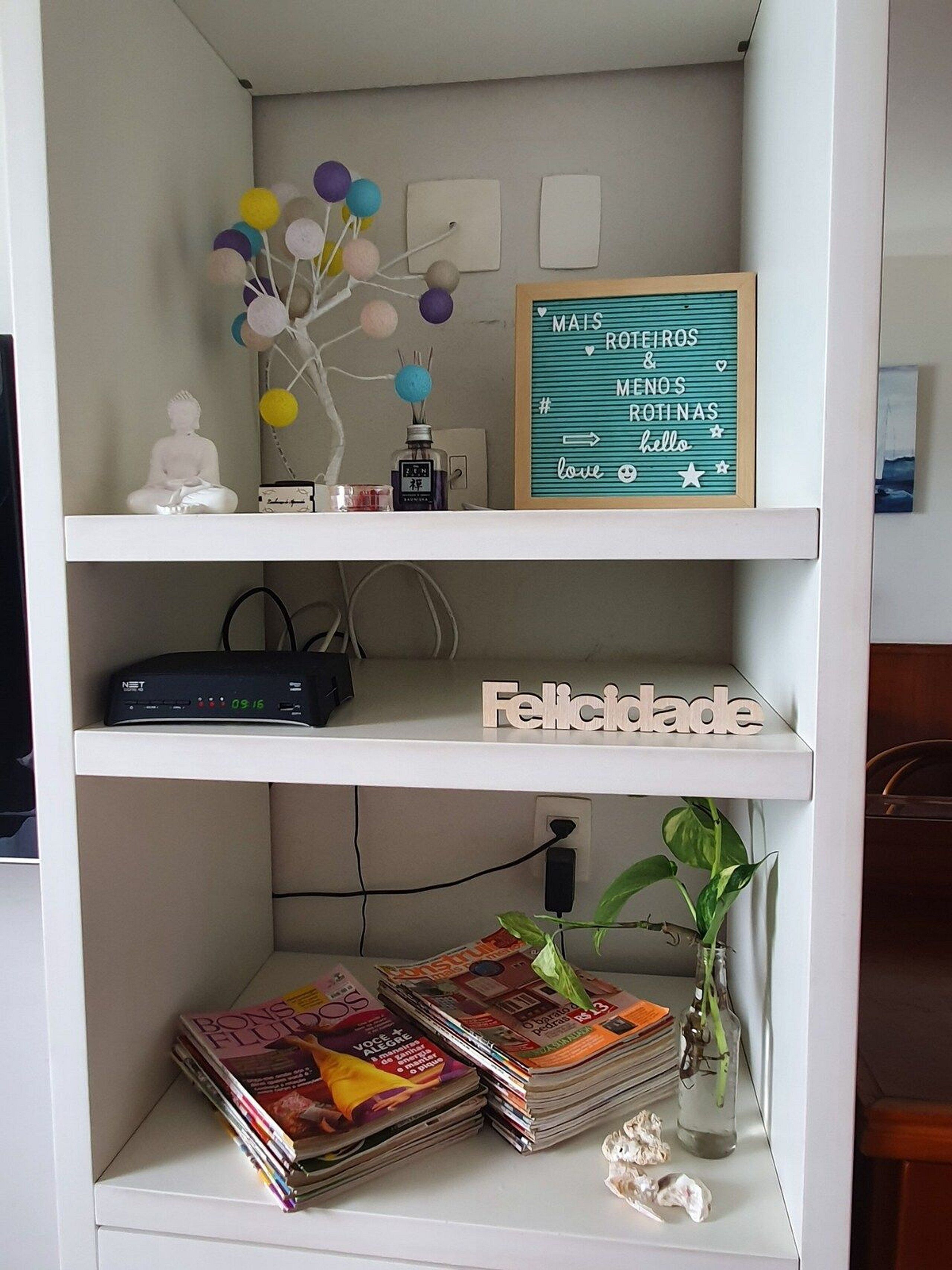 A white shelf with a Buddha statue, a decorative tree with colorful balls, a framed sign with text, a clock, and a plant.