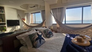 Une chambre avec un lit, une télévision, une bibliothèque et une vue sur la mer.