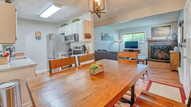 Una cocina moderna con armarios blancos, un refrigerador de acero inoxidable y un comedor con mesa y sillas de madera.