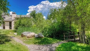 Un sendero conduce a una casa rodeada de exuberante vegetación y un puente de madera.