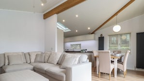 Una sala de estar moderna con un sofá seccional, un comedor con mesa y sillas, y una cocina al fondo.