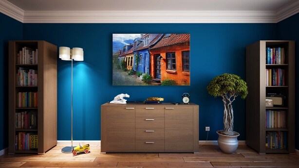 A room with a blue wall, a wooden cabinet with drawers, a floor lamp, a potted plant, and two bookshelves filled with books. - dfdfdfdfdfd (Amritsar)