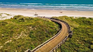 A wooden boardwalk curving through a grassy area leading to a beach.