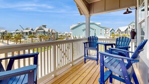 A wooden deck with blue Adirondack chairs and a white railing overlooking a residential area with houses and palm trees.