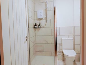 Kylpyhuone, jossa on suihku, wc ja hylly, jossa on hygieniatuotteita.