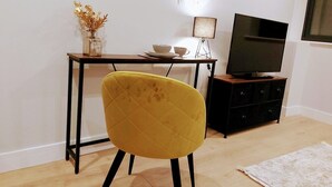 Una stanza con una sedia gialla, una scrivania con lampada, una TV su un mobile e un piccolo armadietto.
