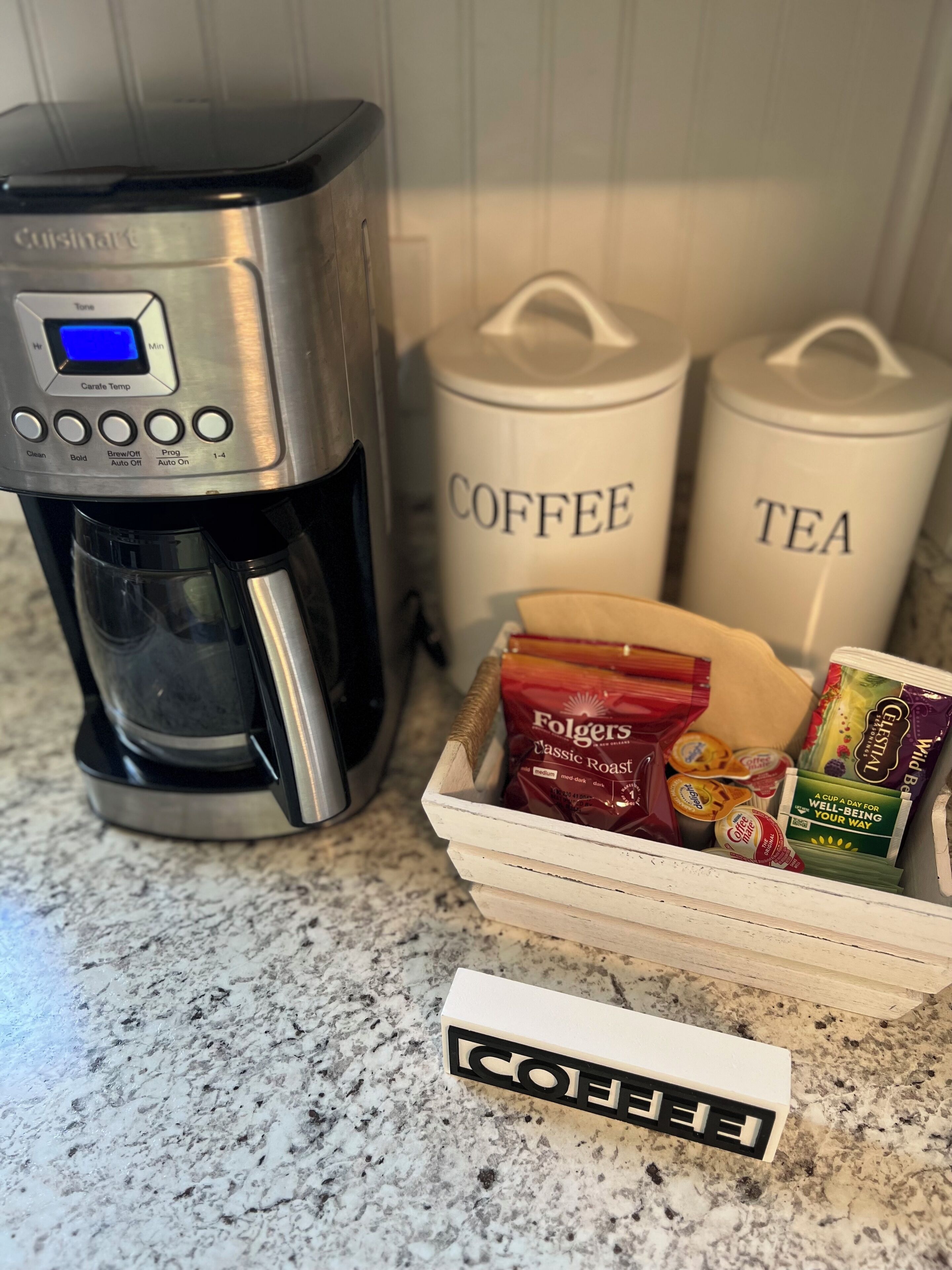 Une machine à café, des récipients pour le café et le thé, et un panier contenant des dosettes de café et du lait en poudre.