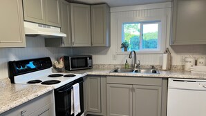 A kitchen with a white stove, a microwave, a sink, and cabinets. - Cozy Sunset Cottage on the family farm near Cave Run Lake and Morehead State  (Morehead)