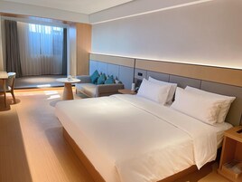 Habitación de hotel moderna con una cama grande, un área de descanso con una mesa y vistas a través de una ventana con cortinas.