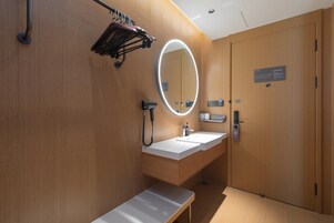Un baño moderno con un tocador de madera, un banco, un espejo con luz y una puerta con un letrero.