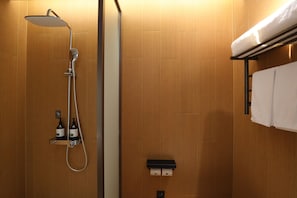 Ducha con cabezal de ducha de mano y grifo empotrado en la pared. Hay dos botellas de champú y acondicionador en un estante debajo de la ducha.