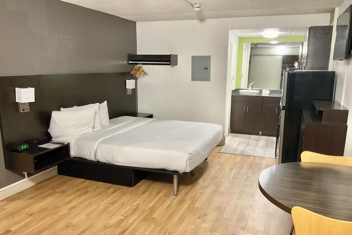 A hotel room with a bed, bedside table, nightstand, and a small desk with a chair.