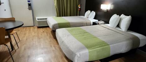 Ein Hotelzimmer mit zwei Betten, einem kleinen Tisch, einem Stuhl, einem Heizgerät, einer Tür und einer Wandleuchte.