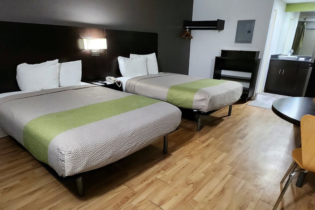 A hotel room with two beds, a desk, a chair, a wardrobe, and a mirror.