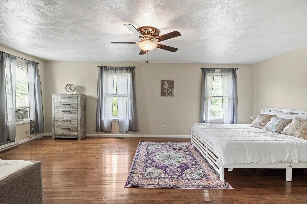 Une chambre à coucher avec un lit, un ventilateur de plafond, une commode et une fenêtre avec des rideaux.