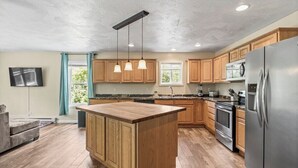A modern kitchen with wooden cabinets, a central island, stainless steel appliances, and pendant lighting.